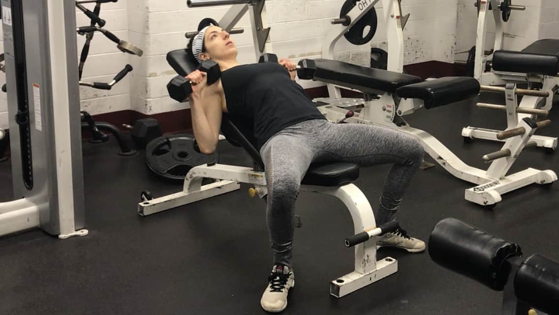 brittany lying on an incline bench holding a dumbbell in each hand that she is holding up by her chest