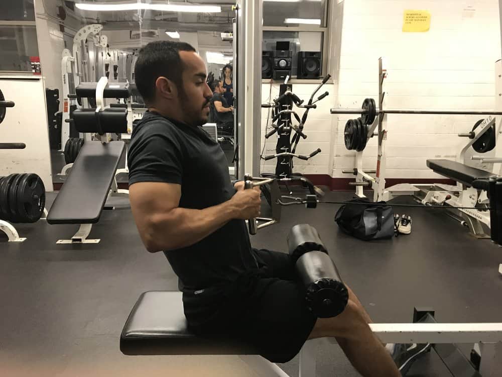 alex on a seated cable row machine showing bad posture by shrugging his shoulders as he pulls the weight toward his abdomen