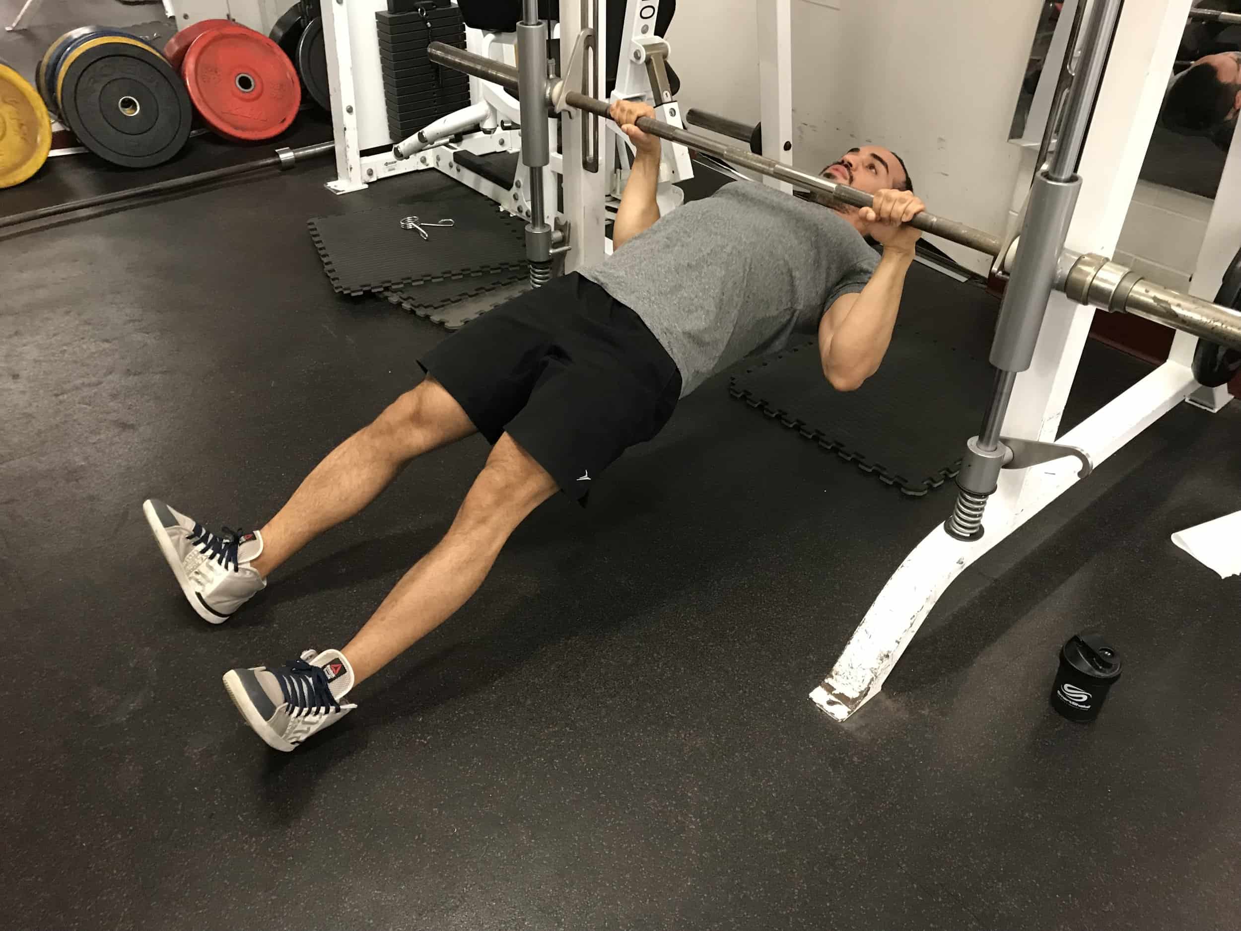 alex at the top part of a horizontal pullup hanging from a barbell with his back parallel to the ground and feet straight