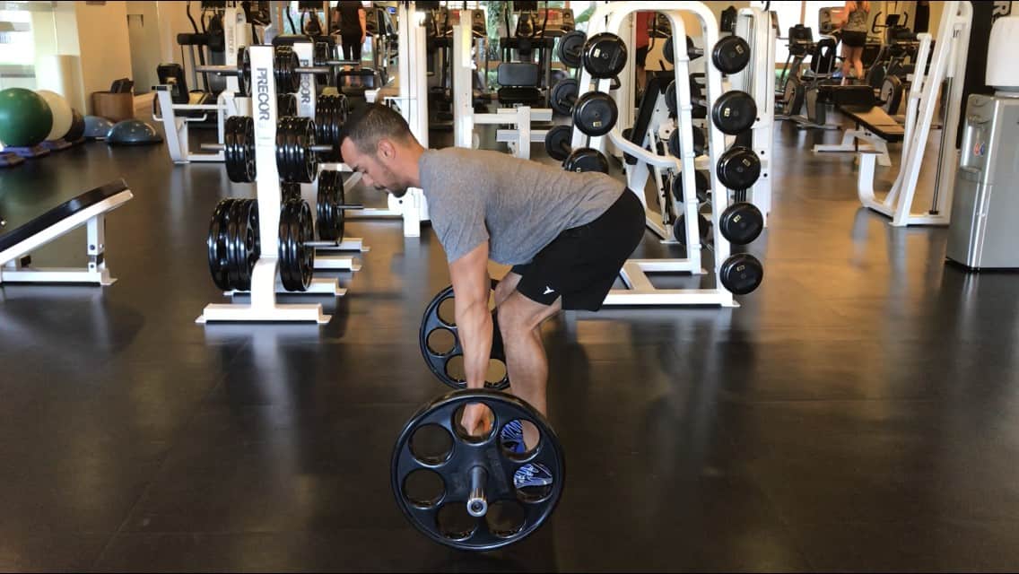 alex at the bottom of the barbell row: bent over, back flat, knees slightly bent, and grabbing the barbell which is on the floor - side view