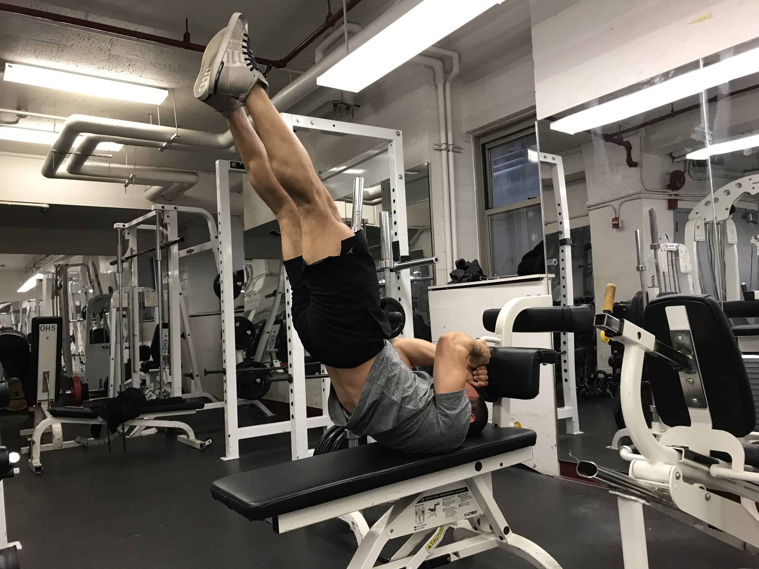 alex on his back holding onto something behind him while lifting his legs and torso straight up to the sky without bending at the hips