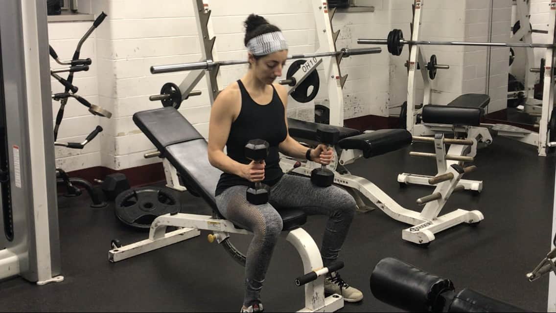brittany sitting on a bench holding a dumbbell in each hand supported on her knees