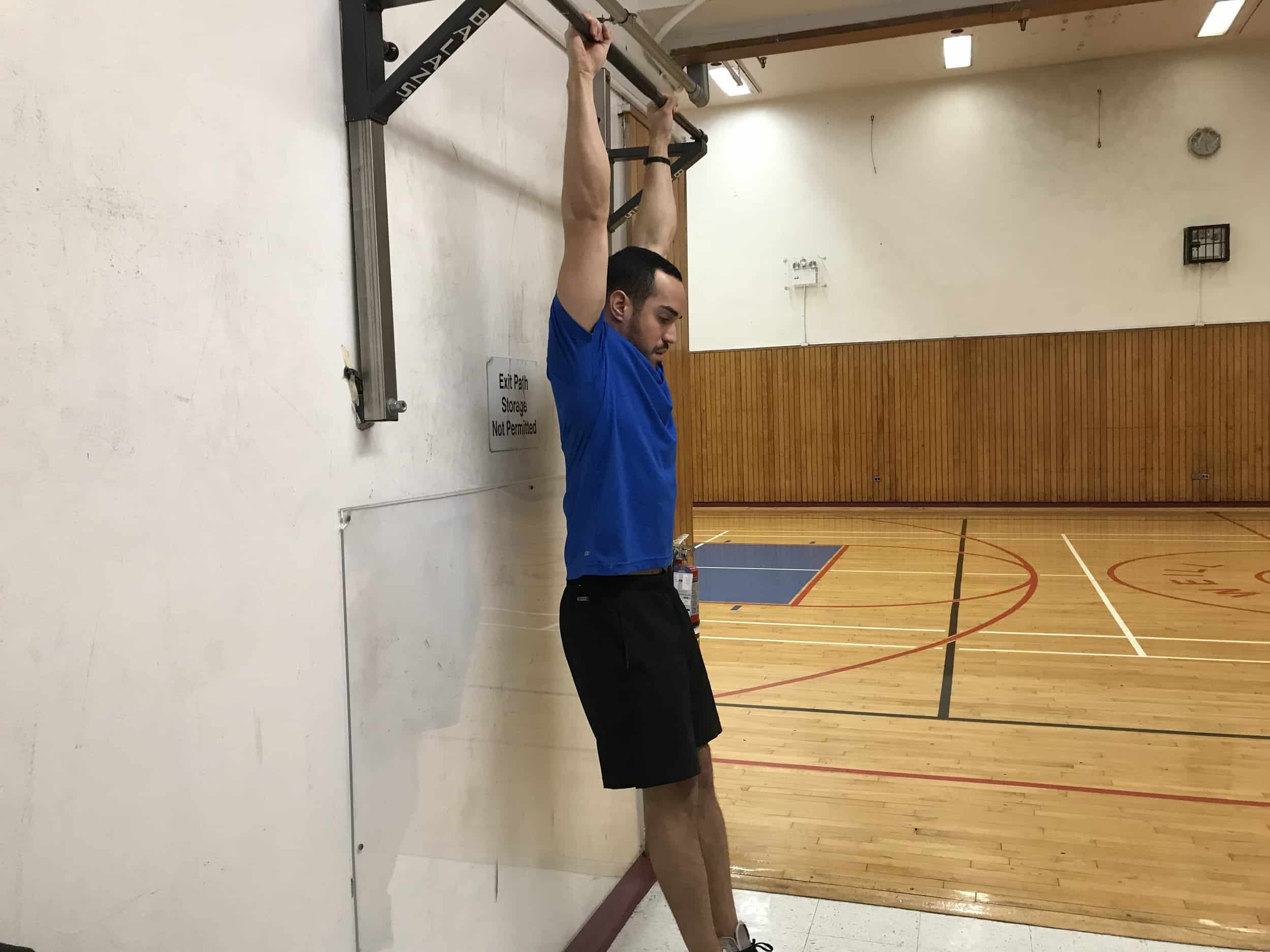 alex showing posterior pelvic tilt while hanging from a bar (lower back is neutral and feet are slightly forward)