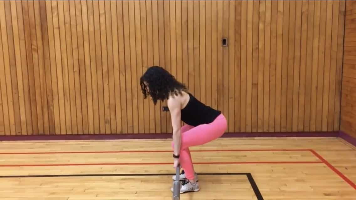 side view of brittany in the bottom of the deadlift keeping the barbell close to her as shins as she is bent over with a flat back and shins relatively vertical