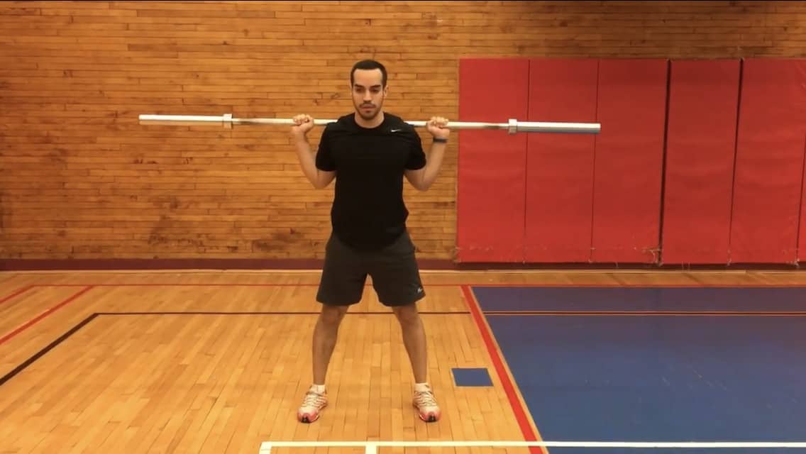 alex at top of a squat holding a barbell on his back- stance is wider than shoulder-width
