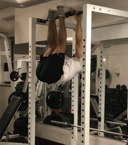 alex at the top of the toes to bar position: hanging from a bar and his feet touching the bar