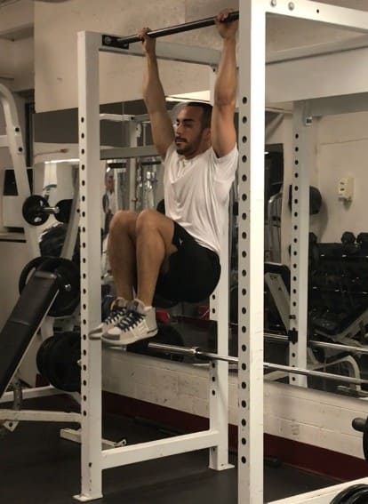 hanging knee raise variation: alex hanging from a bar with his knees tucked up to his chest