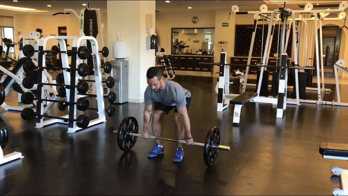 alex at the bottom of the barbell row: bent over, back flat, knees slightly bent, and grabbing the barbell which is on the floor - front view