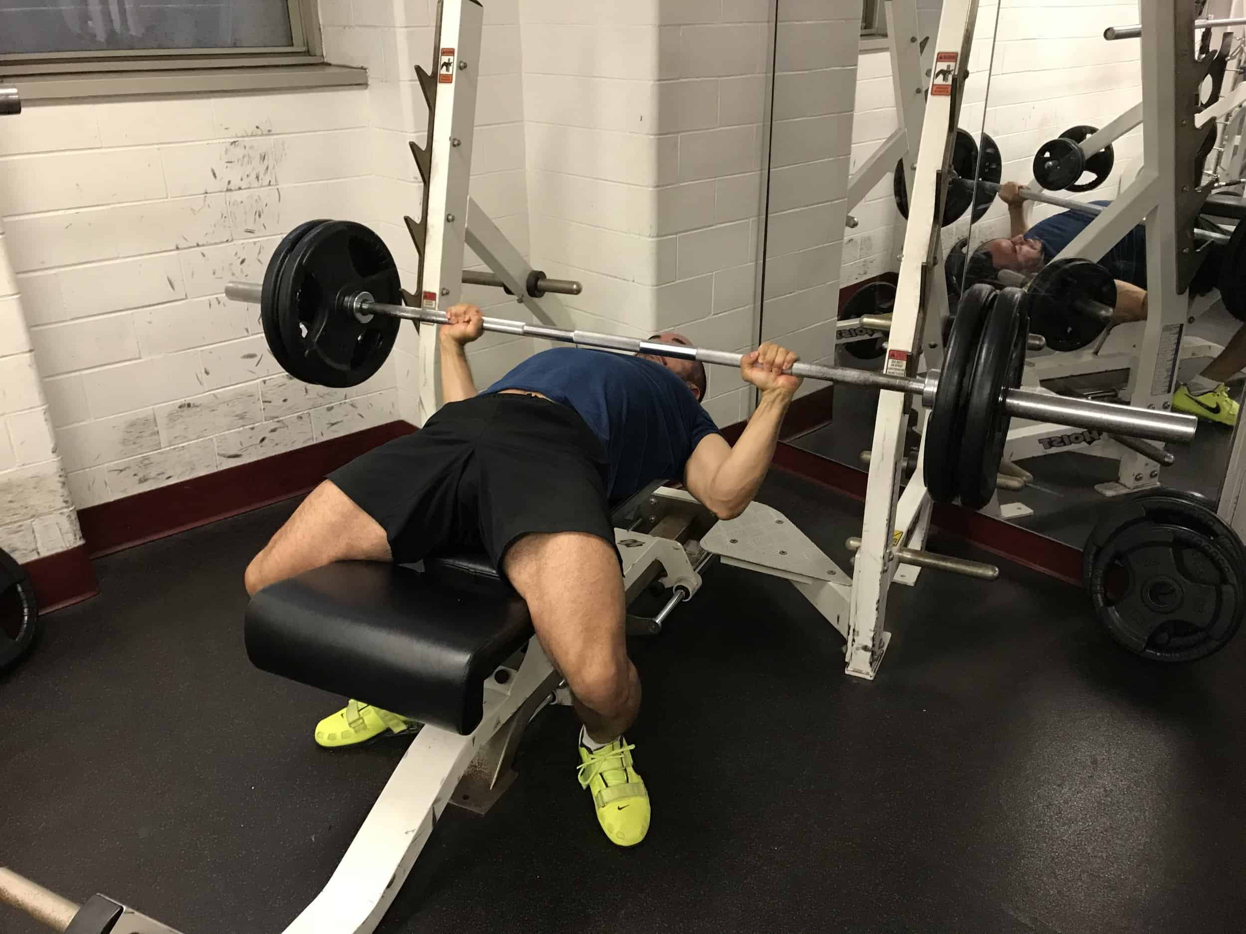 alex on a bench press with the barbell on his chest and his elbows tucked close to the body