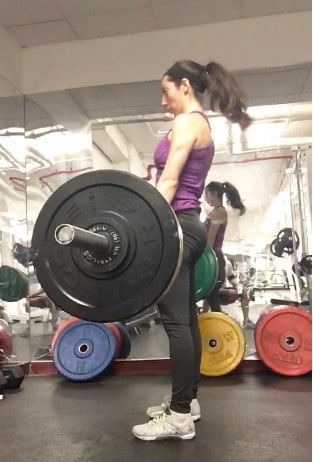 brittany standing up with a barbell close to her thighs after doing a deadlift