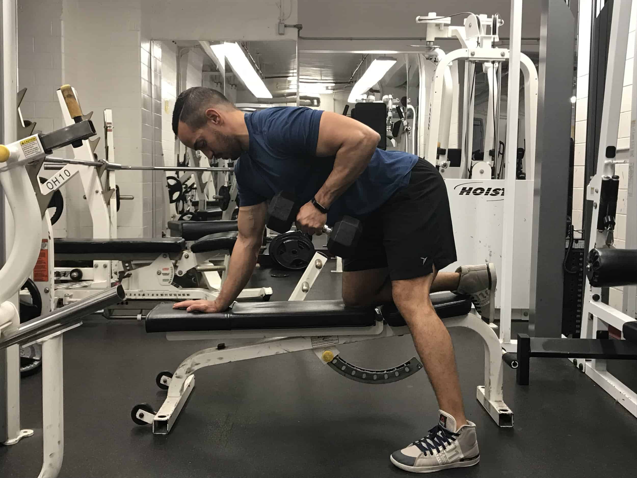 how-to-do-one-arm-db-row- top position of the exercise- alex kneeling over on a bench with dumbbell pulled up towards abdomen