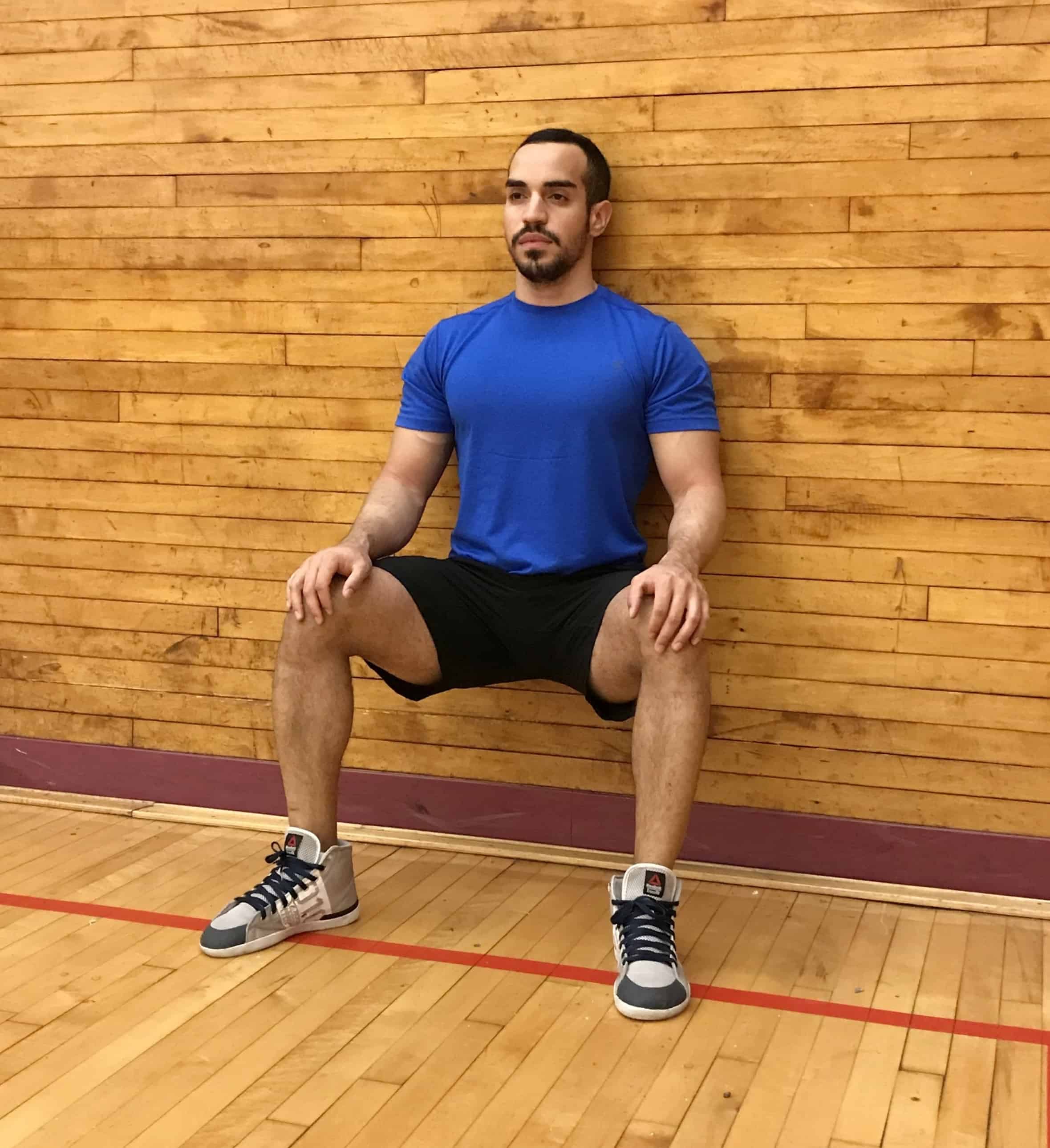 alex sitting against a wall with his back flat against the wall and knees bent at 90 degrees - front view