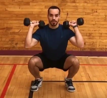 alex at the bottom of a squat holding two dumbbells up on his shoulders
