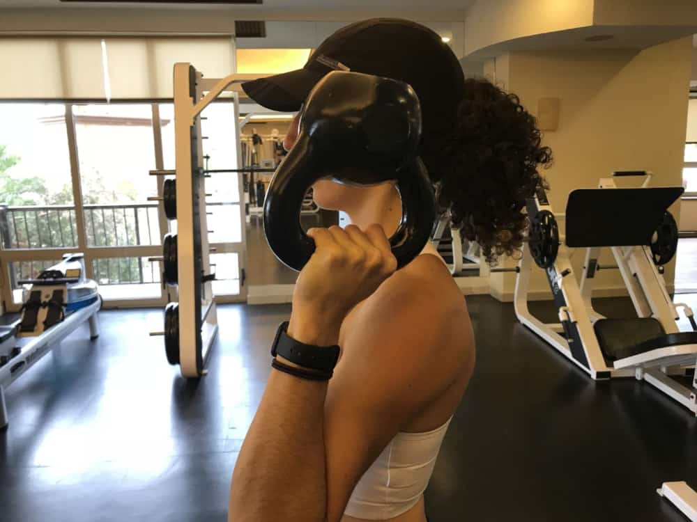 brittany holding a kettlbell in her left arm up by her shoulder with the handle facing down and the bell facing the ceiling