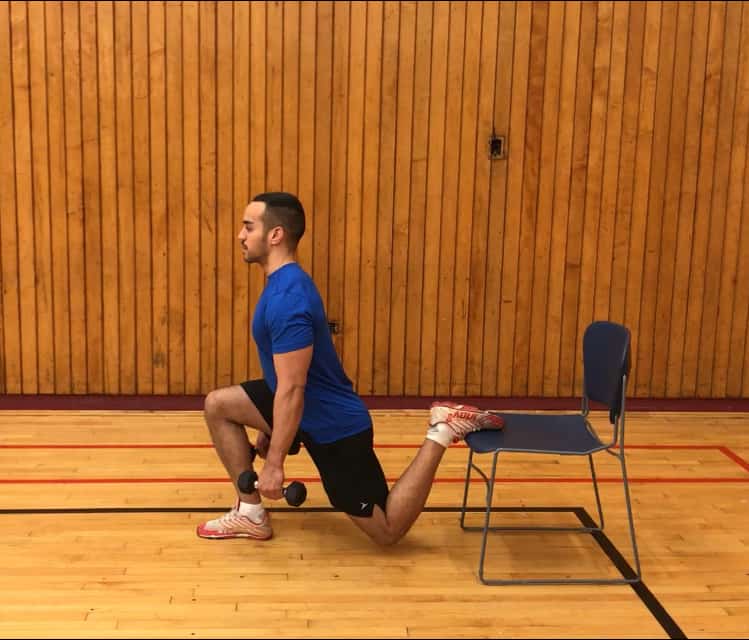 alex kneeling down with his back foot elevated on a chair holding a dumbbell in each hand