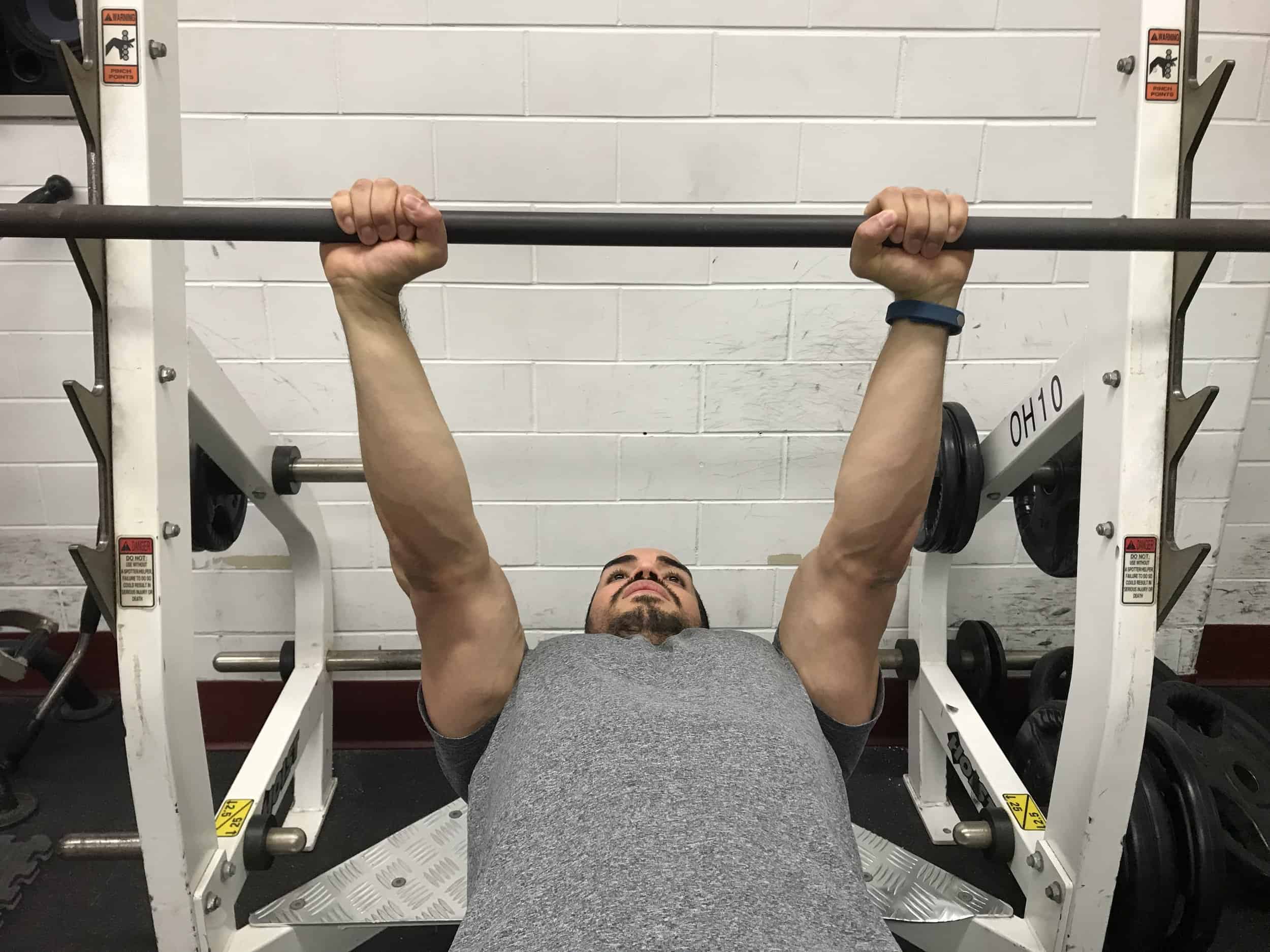 alex at the top of a close grip bench: lying on a bench with the barbell in his outstretched arms