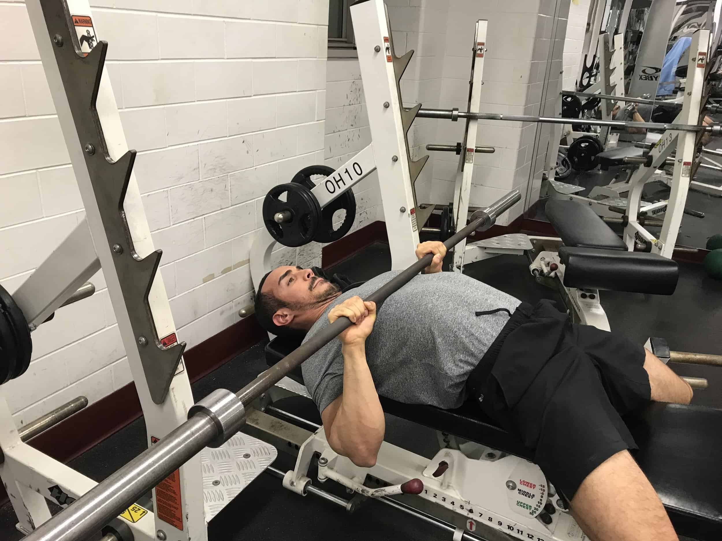 alex at the bottom of a close grip bench: lying on a bench with the barbell touching the lower chest and elbows tucked closed in to the body
