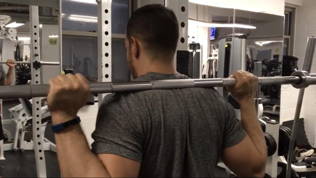 alex with a barbell resting on his upper back under his trap muscles