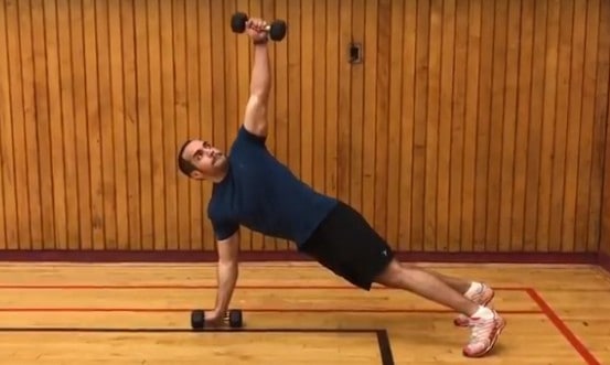 alex rotating his upper body up from a push up position as he lifts one dumbbell straight up to the sky