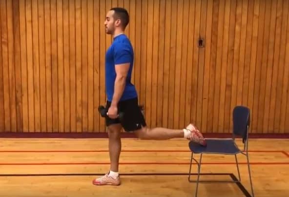 alex standing tall with his back foot elevated on a chair holding a dumbbell in each hand