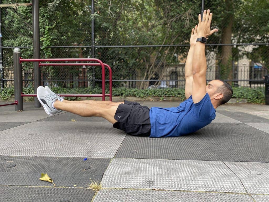 alex lying on her back with his lower back flat on the ground with his arms up towards the skey and legs straight and off the floor- the modified hollow-body-hold-exercise